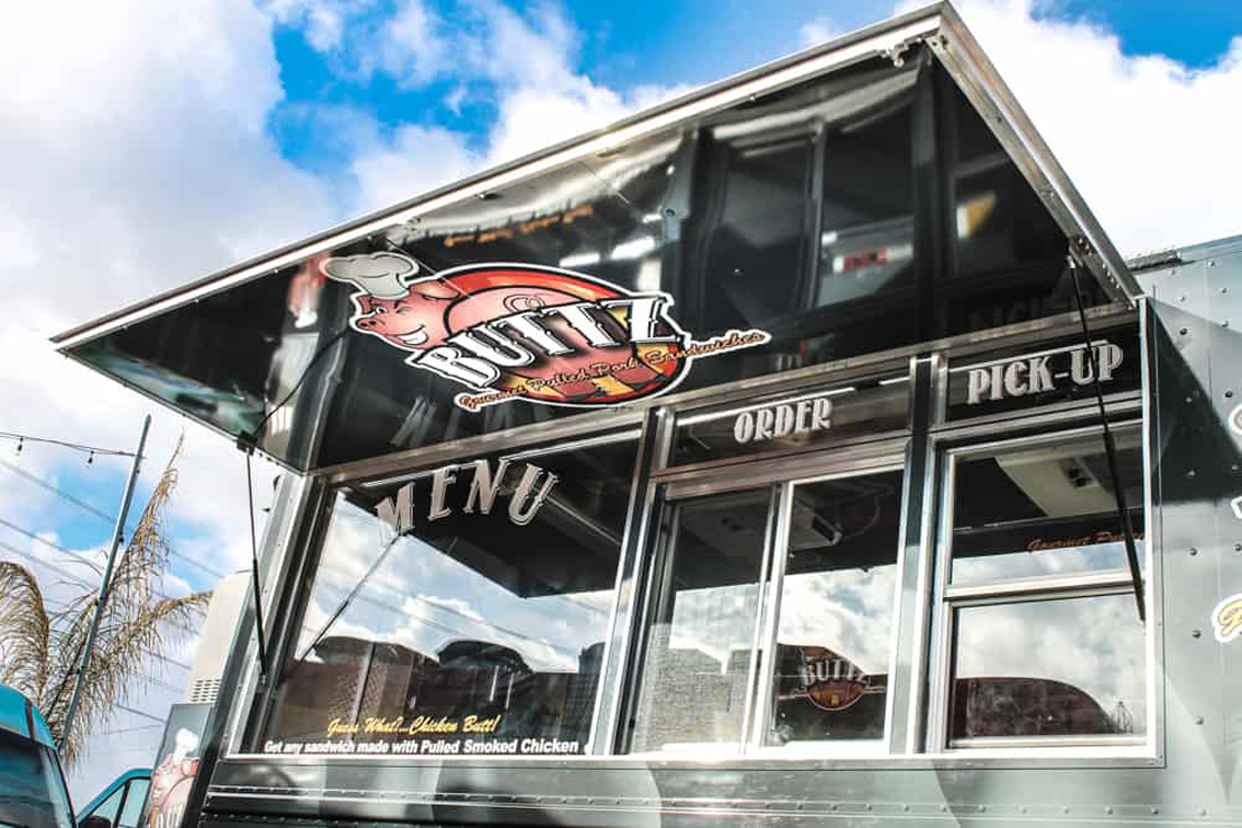 Buttz BBQ Food Truck is custom built by Cruising Kitchens with top of the line equipment, specializing in gourmet pulled pork sandwiches. This simple yet efficient setup features a smoker, quick warmer top of the line friers, and with their eye-catching winking pig logo, the wrap package used capitalized on this and building a social following. What is unique about this