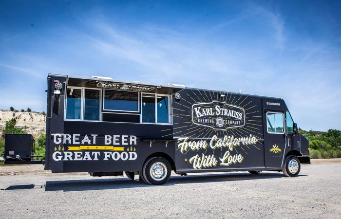 The Karl Strauss Food Truck is a unique mobile kitchen built by Cruising Kitchens, featuring the Karl Strauss logo with beautiful San Diego skyline backdrops. This top-of-the-line food truck comes equipped with commercial appliances for a quality culinary experience.